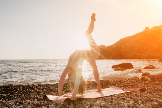 Woman sea yoga. Happy woman with black hair doing Pilates with the ring on the yoga mat near the sea on the pebble beach. Female fitness yoga concept. Healthy lifestyle, harmony and meditation. photo
