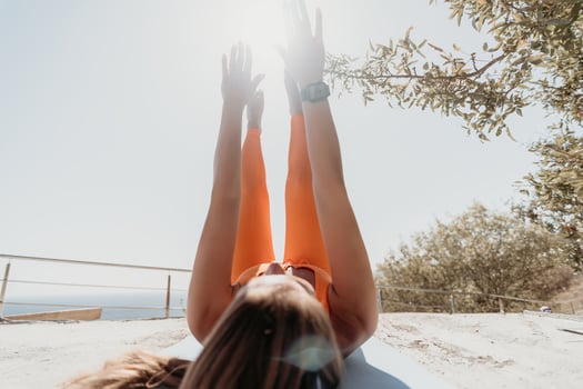 Fitness woman sea. Happy middle aged woman in orange sportswear exercises morning outdoors on yoga mat with laptop in park over ocean beach. Female fitness pilates yoga routine. Healthy lifestyle. photo