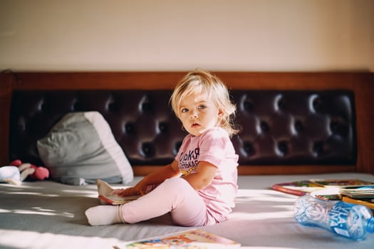 Little girl with colorful books sits on the bed photo