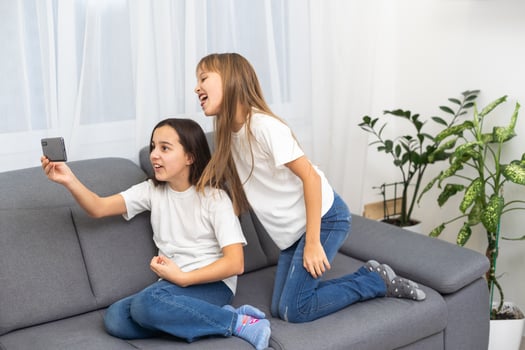 people, technology and friendship concept - happy teenage girls taking selfie with smartphone sitting on sofa at home photo