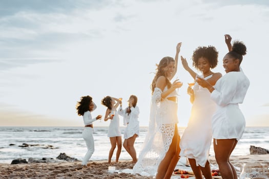 Group of carefree young women toasting wine glasses while dancing and having fun on the beach, having hen party at coastline. Female friends enjoying their vacation photo