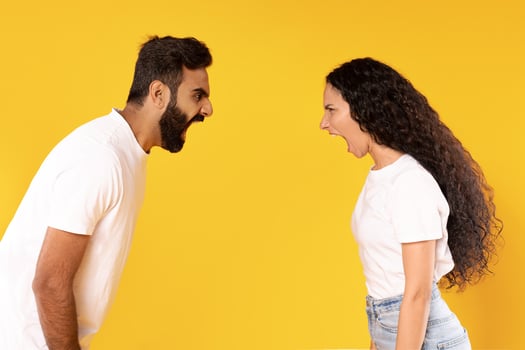 Family Problems, Conflicts. Mad Arabic Couple Shouting At Each Other Having Quarrel Standing On Yellow Background. Side View Of Angry Young Spouses Freaking Out And Yelling Loudly During Scandal photo