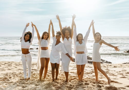 Joyful multiracial women with hands up posing on the beach, having fun and dancing, enjoying hen party outdoors on ocean shore, full length photo
