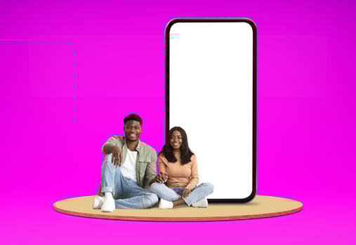 Relaxed positive happy millennial black man and woman lovers chilling on platform next to huge phone with white empty screen, showing nice dating mobile app, colored background, mockup, blank space photo
