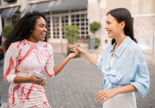 Portrait Of Two Cheerful Multhiethnic Female Friends Laughing And Chatting Outdoors, Joyful Beautiful Young Girlfriends Meeting On City Street, Happy To See Each Other, Having Fun Outside photo
