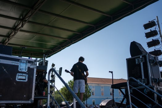 Anonymous male artist playing guitar on stage in city under blue sky photo