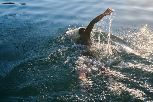 Triathlon athlete swimming on lake in sunrise wearing wetsuit photo