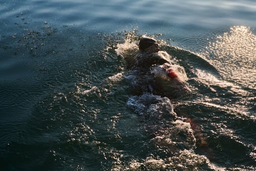 Triathlon athlete swimming on lake in sunrise wearing wetsuit photo