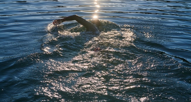 Triathlon athlete swimming on lake in sunrise wearing wetsuit photo