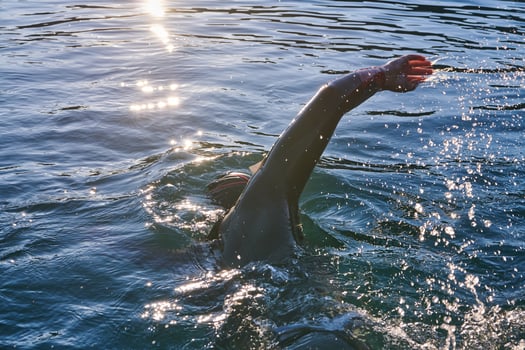 Triathlon athlete swimming on lake in sunrise wearing wetsuit photo