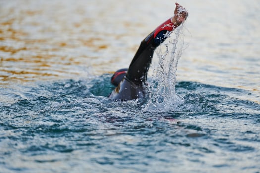 Triathlon athlete swimming on lake in sunrise wearing wetsuit photo