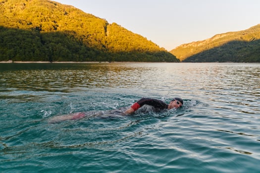 Triathlon athlete swimming on lake in sunrise wearing wetsuit photo