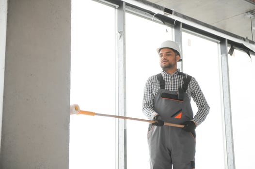 An Indian apartment repair worker paints a white wall with a roller photo