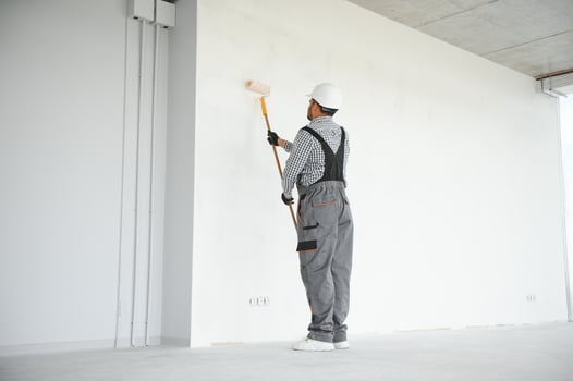 An Indian apartment repair worker paints a white wall with a roller photo