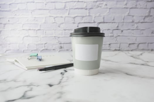 A disposable coffee cup is placed on a marble surface next to a notebook and pen photo