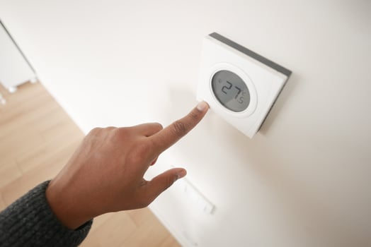 Hand Adjusting Smart Thermostat on White Wall for Optimal Home Temperature Control photo
