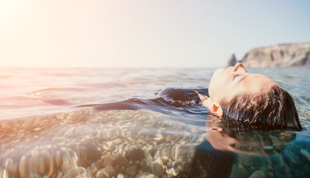 Woman swimming in sea at sunset, float on calm water back view. Concept of body image and fitness, enjoying a serene beach. Happy woman with perfect fit body enjoys sea beach photo