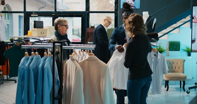 Fashion stylist suggesting clothing items to regular customer, team of store workers help elderly woman to buy trendy clothes on sale. Retail clerks assisting client during shopping spree. Camera B. photo