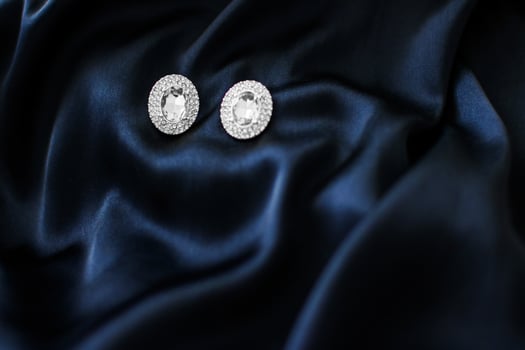 Luxury diamond earrings on dark blue silk background, holiday glamour jewelery present photo