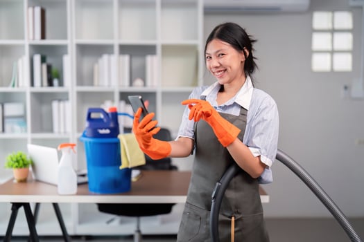 Smiling female office cleaner with vacuum and phone. Concept of workplace multitasking photo
