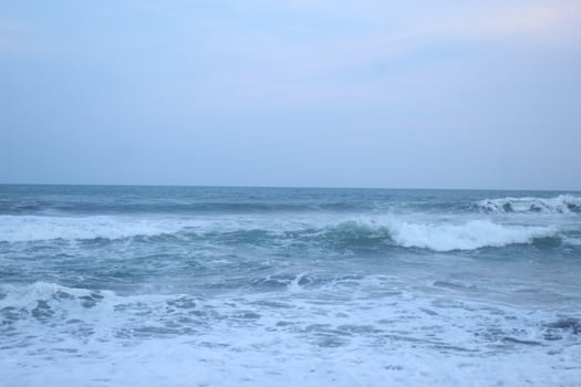 As the tide sweeps in at South Jogja Jetis Beach, Cornwall under a serene sky, waves gently roll, accompanied by ripples and bubbling foam. photo