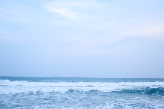 As the tide sweeps in at South Jogja Jetis Beach, Cornwall under a serene sky, waves gently roll, accompanied by ripples and bubbling foam. photo