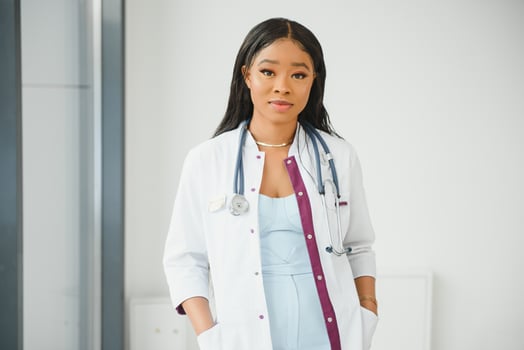Closeup headshot portrait of friendly, smiling confident female healthcare professional with lab coat, arms crossed holding glasses. Isolated hospital clinic background. Time for an office visit photo