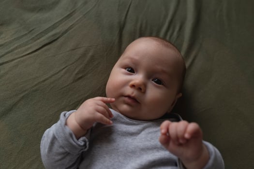 An adorable baby gazes curiously, hands near face, embodying innocence and calm photo