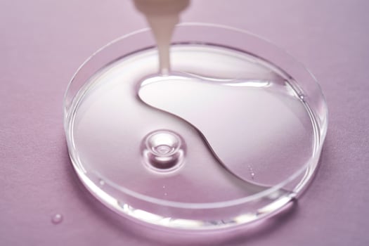 Serum or cosmetic oil flows into a transparent bowl on a purple background. photo