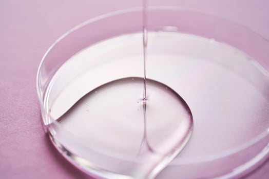 Serum or cosmetic oil flows into a transparent bowl on a purple background. photo