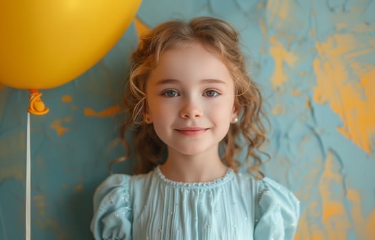 Young girl in a light blue dress holding a yellow balloon on a pastel background, celebrating a birthday photo