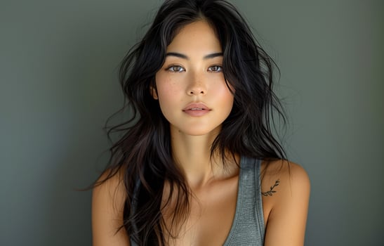 Asian woman with long black hair, wearing a grey tank top, posing for the camera against grey background photo