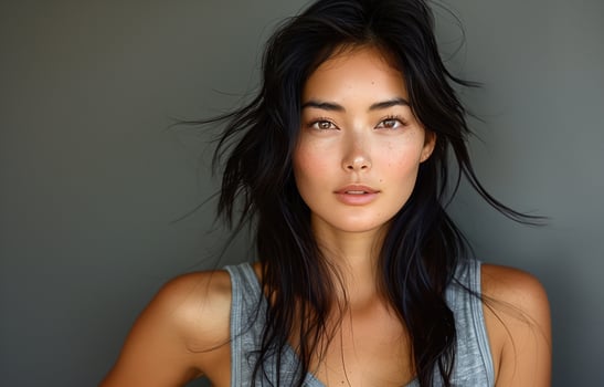 Asian woman with long black hair, wearing a grey tank top, posing for the camera against grey background photo