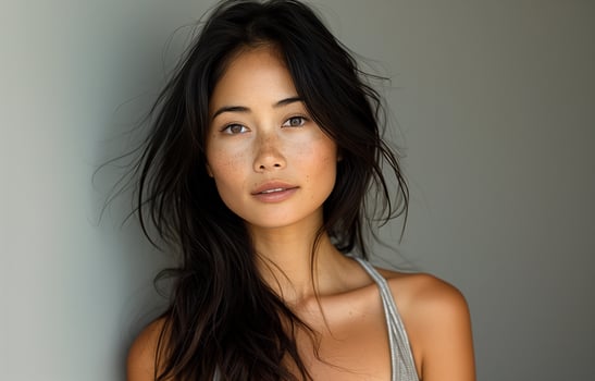 Asian woman with long black hair, wearing a grey tank top, posing for the camera against grey background photo