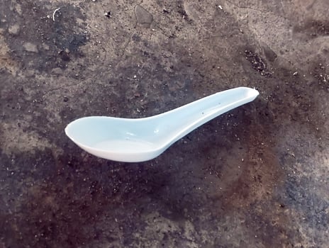 Single white plastic spoon lying on rough floor photo