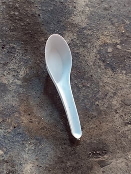 Single white plastic spoon lying on rough floor photo
