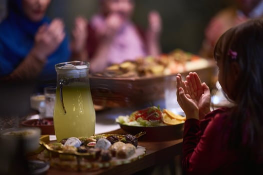 A young girl raises her hands in prayer as she prepares for her iftar meal during the holy month of Ramadan, embodying spiritual devotion and innocence. photo