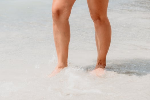 Sea beach travel - woman walking on sand beach leaving footprints in the white sand. Female legs walking along the seaside barefoot, close-up of the tanned legs of a girl coming out of the water. photo