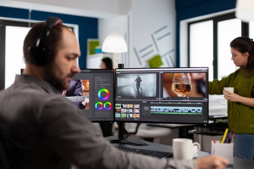 Videographer with headset working with footage and sound on pc with two displays, taking notes while editing customer . Man processing film montage sitting in creative startup agency office. photo