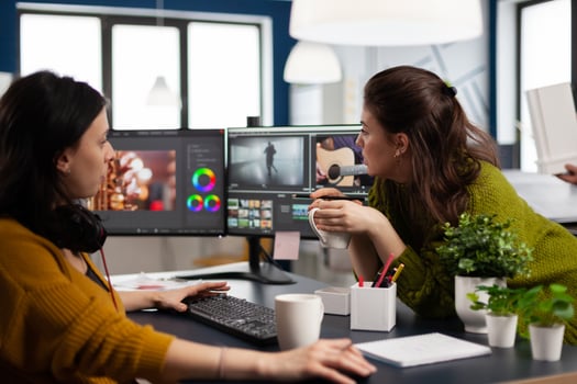 Coworkers editors discussing in front of pc working for client footage using post production software and two monitors. Creative People processing film montage in digital multimedia company photo