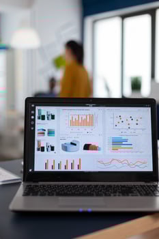 Laptop with marketing charts, graphs analitics in start up company. Workplace area in business center with multi ethnic employees in it, shot of room with modern furniture and blue wall. photo
