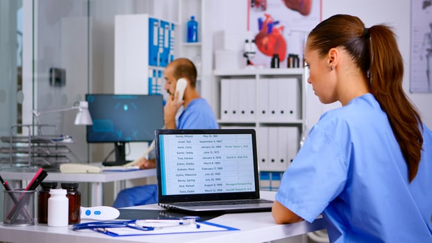 Back view of resident physician checking appointments on laptop while coworker answering at phone offering medical consultation to remote patient, assistant working in hospital clinic photo