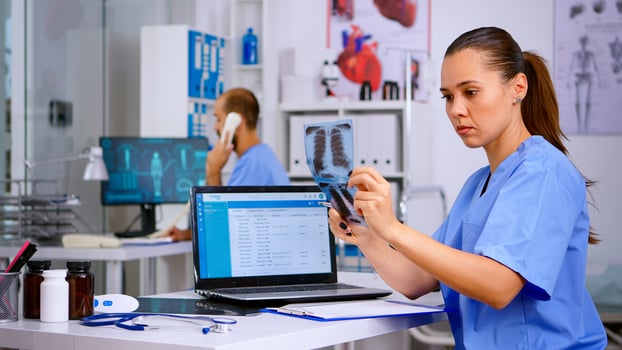 Medical doctor nurse holding and analysing radiography checking treatment of diagnosed patients, writing informations in laptop. Assistant working in hospital making appointments and registration. photo