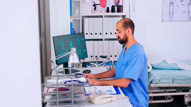 Man practitioner working in medical office with digital body scan, analysing human diseases, health problems. Health care staff sitting at desk in medicine uniform writing treatments photo