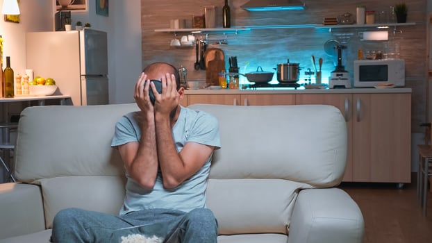 Concentrated man sitting in front of television while watching fun shows series eating snack. Caucasian male relaxing on couch holding popcorn bowl late at night in kitchen photo