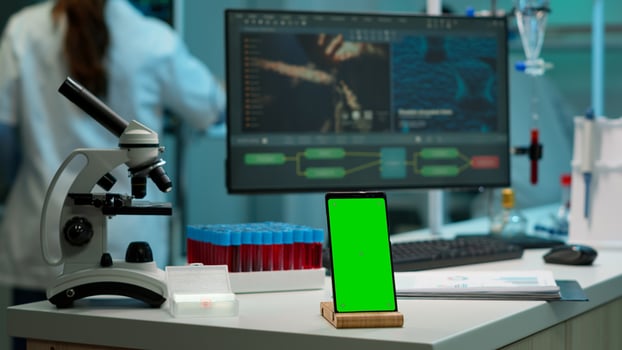Smartphone with green screen working in laboratory with mock up, chroma key display while professional engineer testing virus evolution in background. High tech development lab with blood samples photo