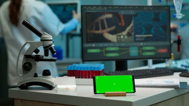 Horizontal mobile phone with green screen working in labooratory with mock up template, chroma key display while professional engineer testing virus evolution in background. High tech development lab. photo