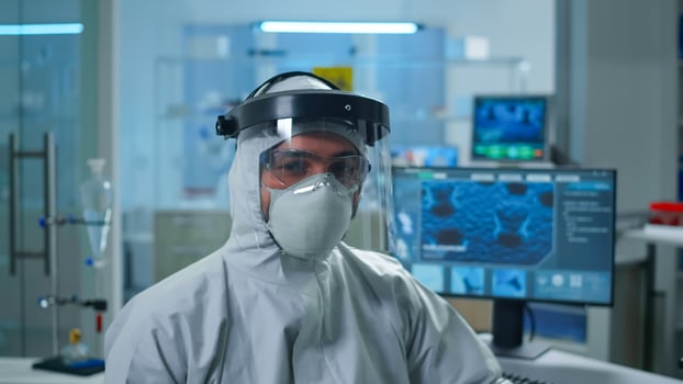 Close up of tired chemist man doctor in coverall looking at camera working in scientific equipped laboratory. Various bacteria, tissue and blood samples, pharmaceutical research for antibiotics photo