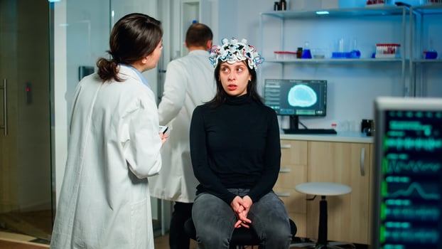 Doctor specialist in neurological medicine typing health informations of patient. Woman wearing eeg headset answering to medical researcher, monitor showing brain scan in equipped laboratory photo