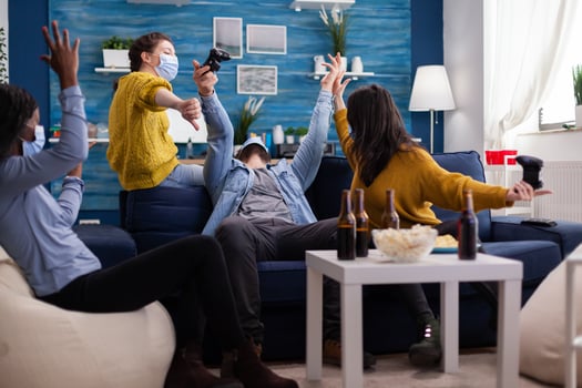 Game over for multicultural friends while playing games using joystick keeping social distancing with face mask due to coronavirus outbreak in the world sitting on couch. photo